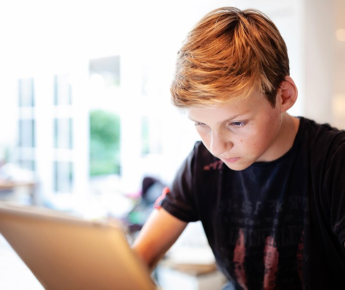 Foto: Een kind in zwart t-shirt geconcentreerd aan het lezen op een laptop in een lichte ruimte.