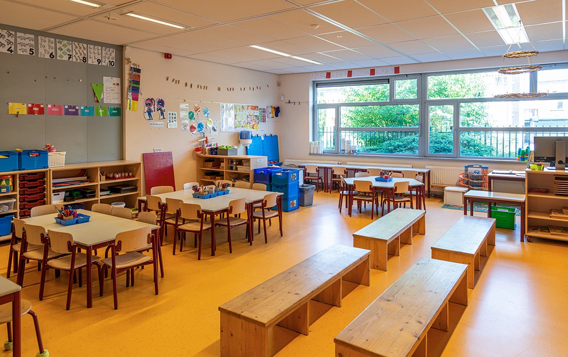 Een kleurrijk en uitnodigend klaslokaal in een basisschool, ingericht met tafels, stoelen en materialen voor creatieve en leerzame activiteiten.